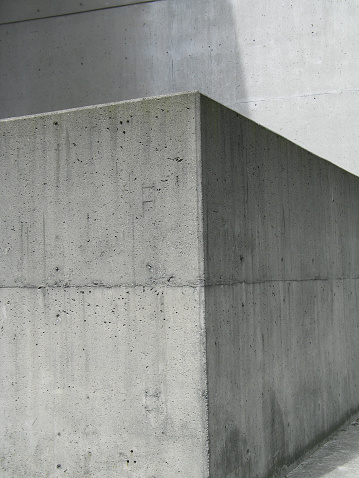 Gray concrete structure with a 90 degree angle in front of a cement wall 