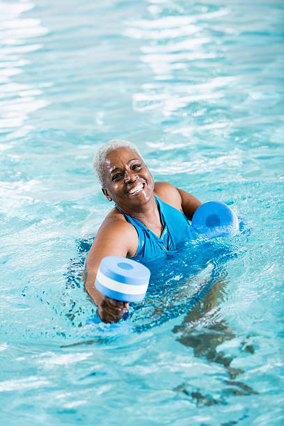 femme noire âgée, faire de l'exercice de gymnastique aquatique - health spa swimming pool relaxation indoors photos et images de collection