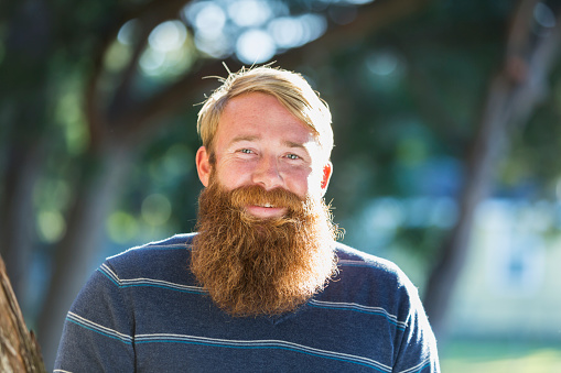 Handsome man with blond hair and a long red beard, standing outdoors on a sunny day.