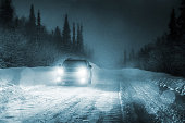 Car driving in forest with headlights lighting snowy road