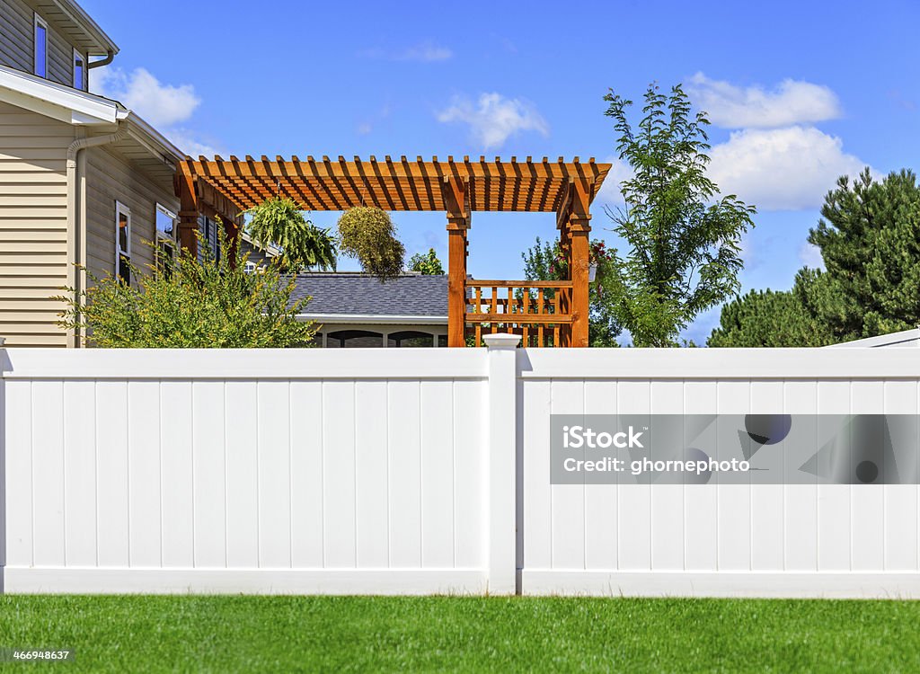 White Vinyl Fence A modern middle class home with its backyard being enclosed for privacy by a new, modern style white vinyl fence. Green grass, and blue sky is in the background. Fence Stock Photo