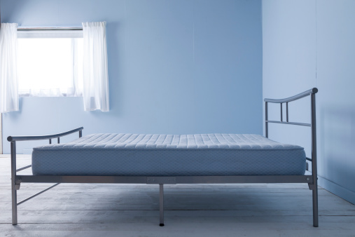 Blue and white study of a mattress on a metal bed in a bare-floorboarded bedroom.
