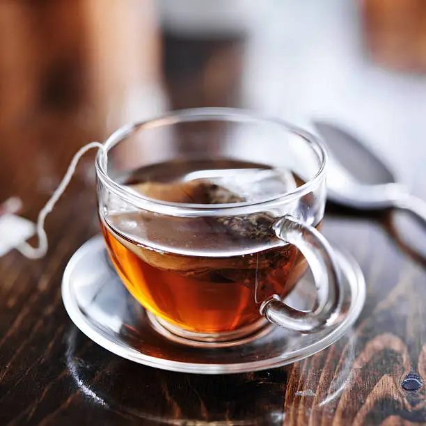 hot cup of tea steeping in glass on wooden table in natural light