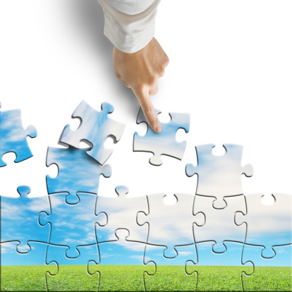 Hand assembling puzzle with beautiful landscape isolated in white background