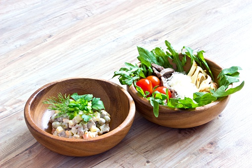 Two kinds of salads in wooden bowls: with vegetables and with beef tongue. Selective focus on wooden background