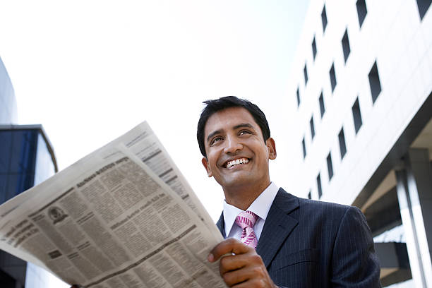 Businessman Reading Newspaper Outdoors Happy young businessman reading newspaper outside office building Indian Newspaper Day stock pictures, royalty-free photos & images