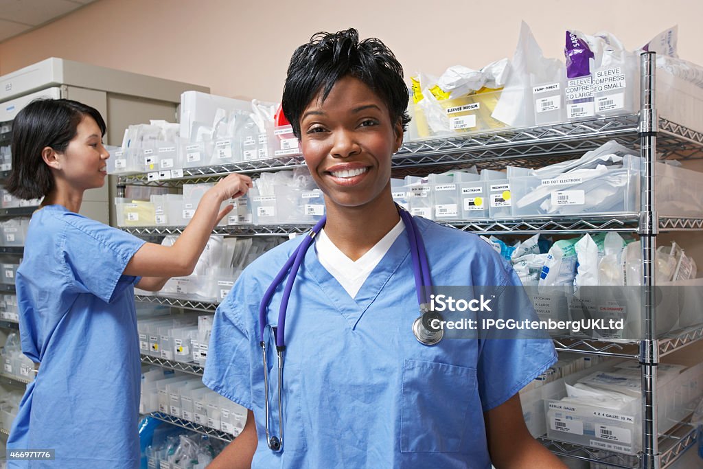 Smiling medical professional and working staff in background Portrait of female doctor, nurse standing by shelves with medical supplies in background Medical Supplies Stock Photo
