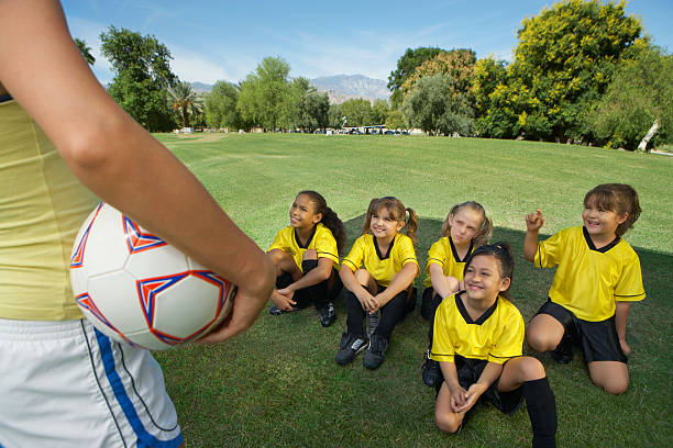 Coach standing in front of group of girl soccer players (7-9 years) sitting on lawn, elevated view
