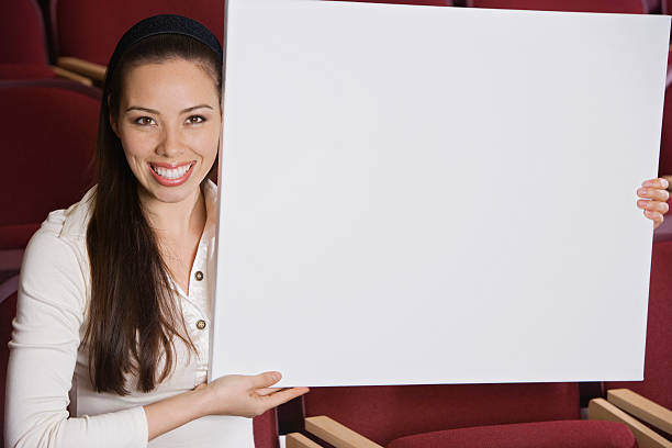 Woman sitting in auditorium, holding empty placard