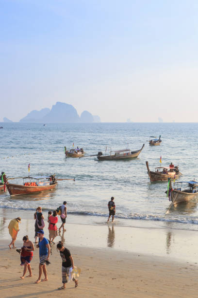 Tourists return from longtail boat trip Aonang, Thailand - January 5, 2014: Tourists returning from a trip with longtail boats at Aonang beach near the city of Krabi, Thailand. The longtail boats are typical for Thailand and are used as water taxis to transport tourists to remote islands and beaches. In the background Poda Island and Chicken Island. koh poda stock pictures, royalty-free photos & images