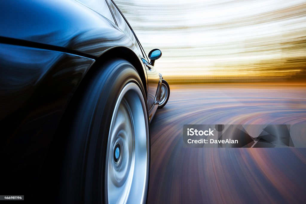 Speeding Curve Sports Car. A black sports car turns in to a corner. Autumn leaves are on the road and in the background blur. Car Stock Photo