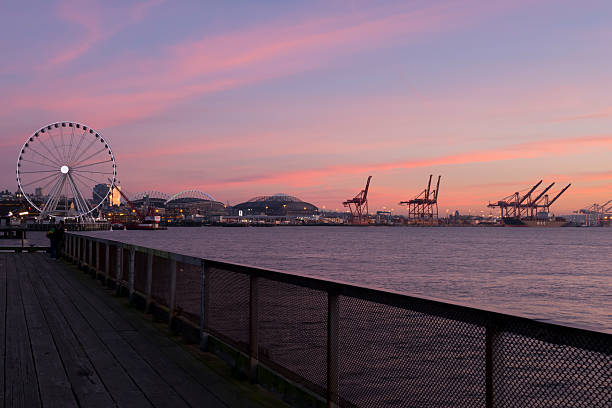 Seattle Sunset Seattle, USA - January 15, 2014: A vivid pink sunset along the waterfront over Elliott Bay with a two people enjoying the view with the stadiums and Ferris wheel in the background.  seattle ferris wheel stock pictures, royalty-free photos & images