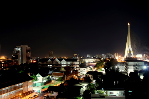 A clear night sky over illuminated buildings in vibrant Bangkok. In the background, Rama VIII bridge is dominating the skyline.