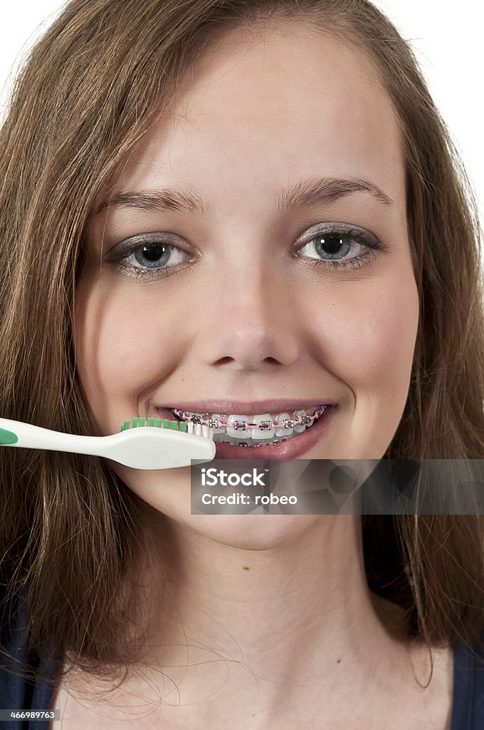 Teen girl with braces brushing teeth A beautiful teenage woman practicing good oral dental care by brushing her teeth Adult Stock Photo