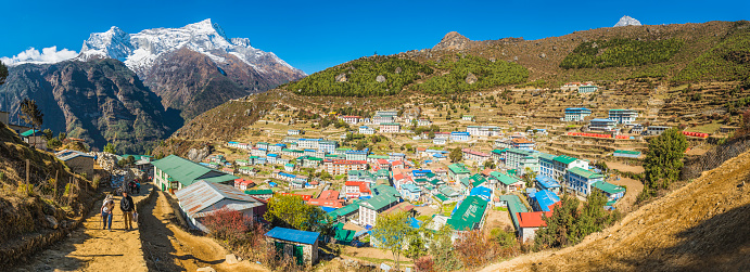 Namche Bazaar, Nepal - 3rd November 2014: Sherpas walking through the iconic village and trading post of Namche Bazaar with its colorful teahouses and lodges crowded into the dramatic mountain amphitheatre high in the Everest National Park of the Nepal Himalaya. Composite panoramic image created from eight contemporaneous sequential photographs. 