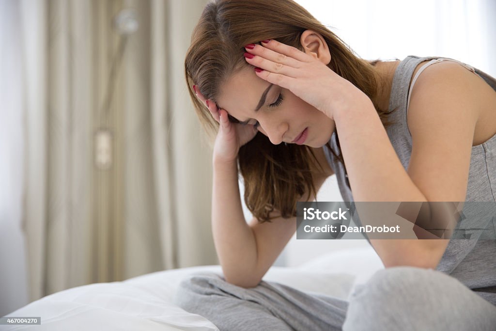 Woman sitting on her bed with her head in her hands Portrait of a pensive woman sitting on the bed at home 2015 Stock Photo