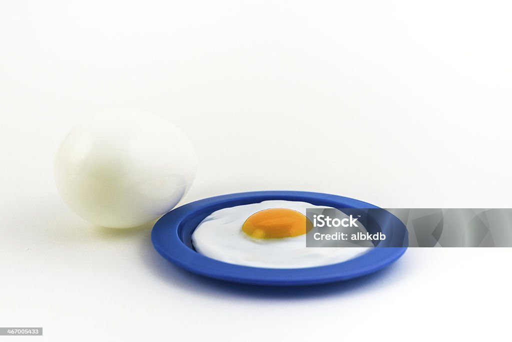 Sunny side up on a plate with a large egg on the side. A toy sunny side up on a blue plate, with a large white, whole egg on the side, isolated against a white background. Plastic Plate Stock Photo