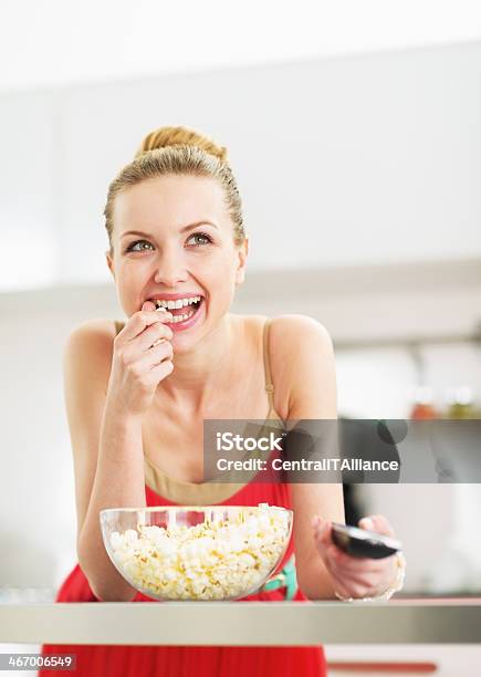 Smiling Young Woman Eating Popcorn And Watching Tv In Kitchen Stock Photo - Download Image Now