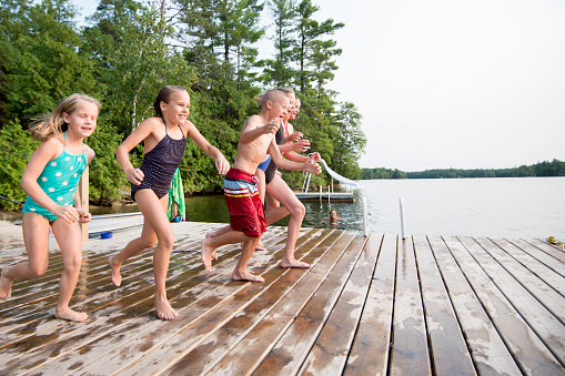 A group of children children running together on a floating dock in a lake on summer vacation.
