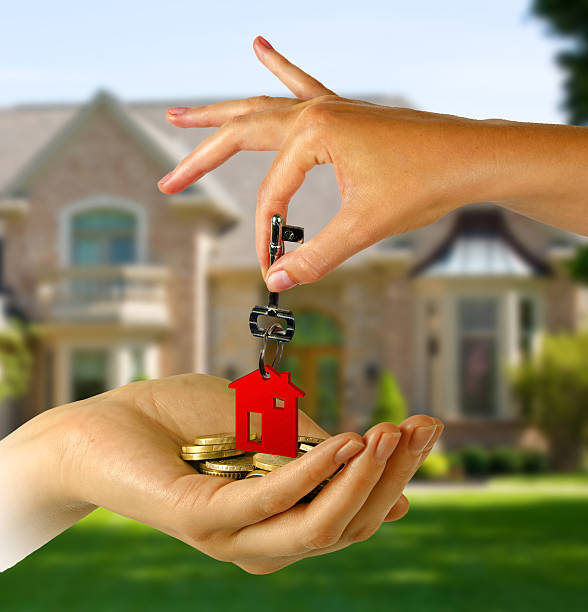 Hand handing over keys with red keychain in front of house stock photo