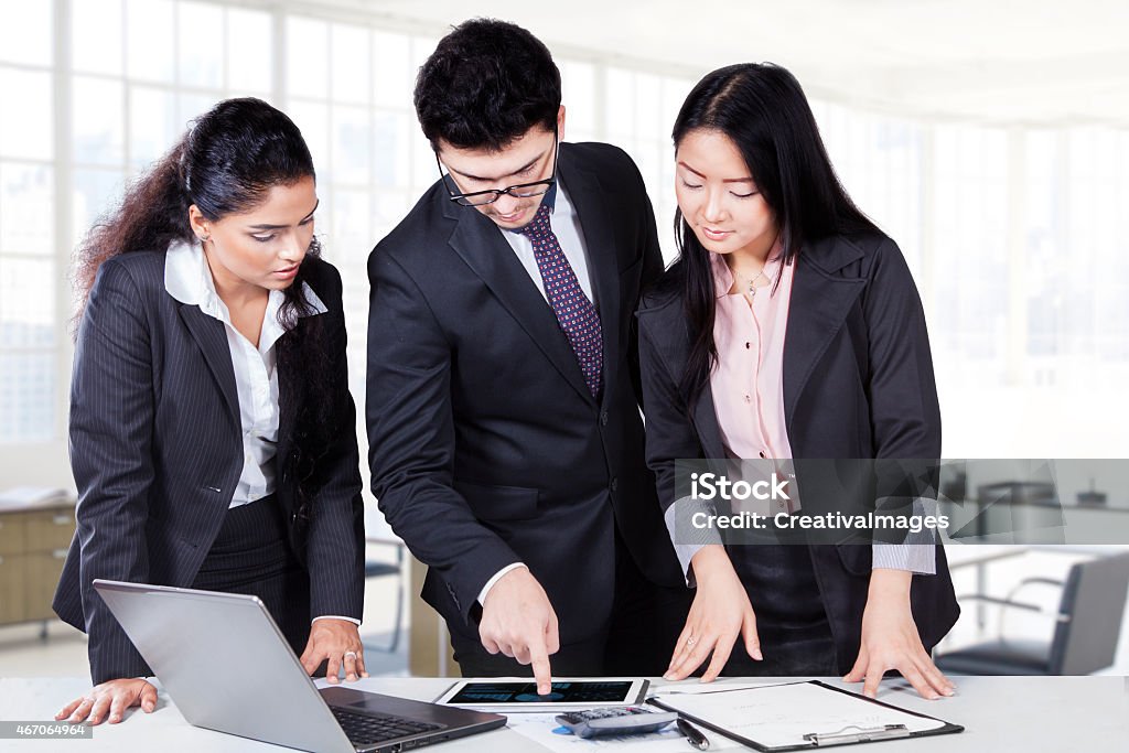 Male manager pointing chart on tablet Young businessman explaining business chart with a digital tablet to his partners in the office Adult Stock Photo