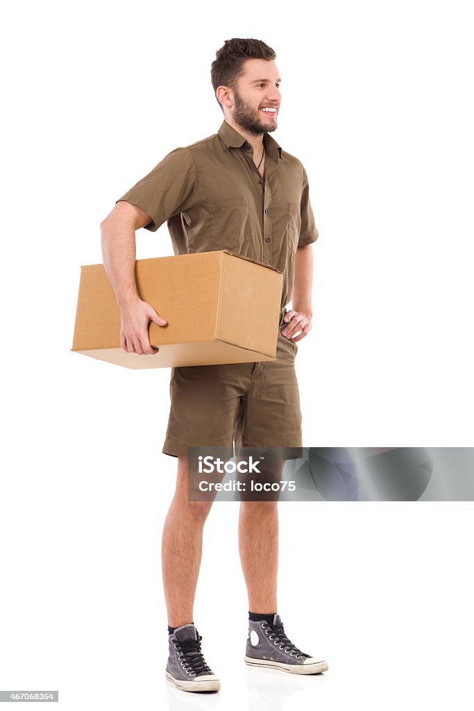 Messenger posing Cheerful courier standing and holding carton box under the arm. Full length studio shot isolated on white. Men Stock Photo