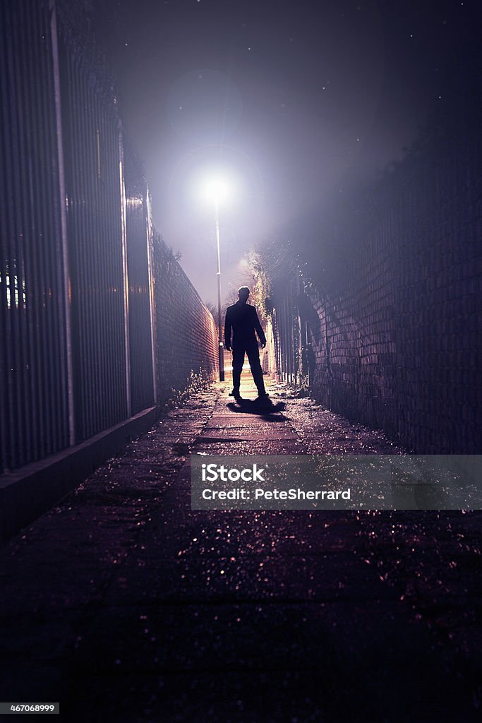 The silhouette of man standing in dark alley. The silhouette of a suited man standing aggressively in a dark alley. Running Stock Photo