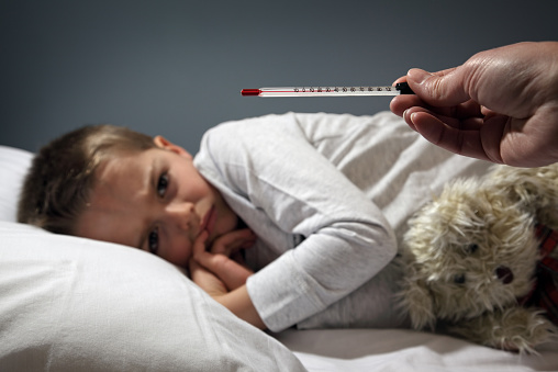 Poorly boy in bed with a thermometer reading high temperature focus on thermometer