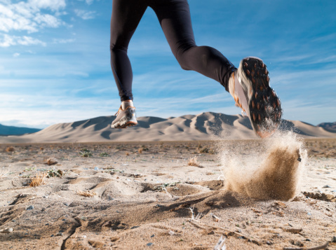 A low angle of a runner in the desert with sand dunes in the horizon.
