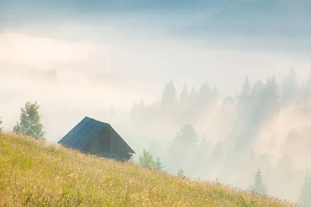 foggy landscape with an old barn in the mountains at the summer