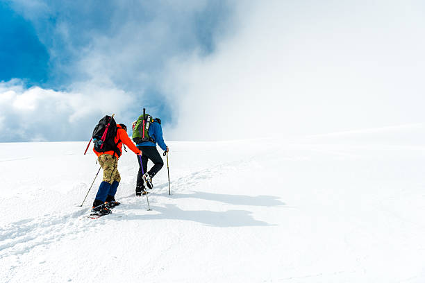 Mountaineering Two mountaineers walking through the mountains covered with snow. snow hiking stock pictures, royalty-free photos & images
