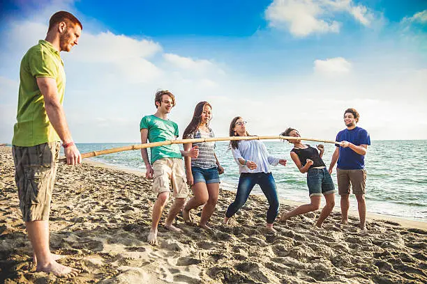 Group of friends playing at limbo game on the beach