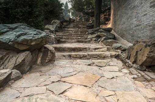 Tall brick wall and long stone staircase in the Beihai Park (near the Forbidden City) in Beijing, China on the Jade Flower Islet. The stairs are leading upwards to the White Dagoba Temple on top of a hill on the island. The Beihai Park used to be an Imperial Park (through five dynasties), but was opened to the public in 1925.