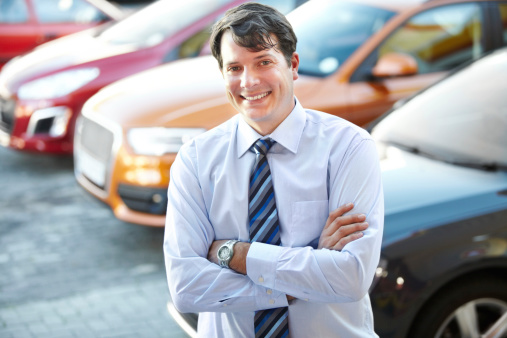 A man smiling confidently while standing in the lot of his dealership
