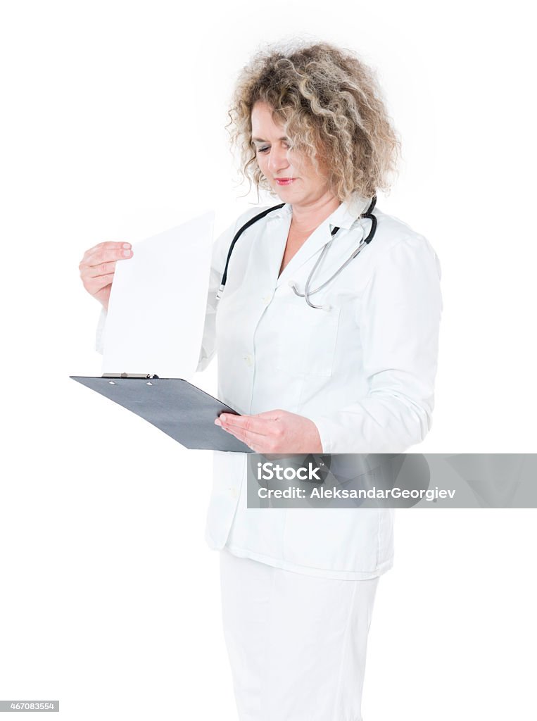 Mature Female Doctor Writing Reading Notes and Working in Uniform Mature Female doctor writing or reading notes and prescriptions on clipboard isolated on white background. 2015 Stock Photo