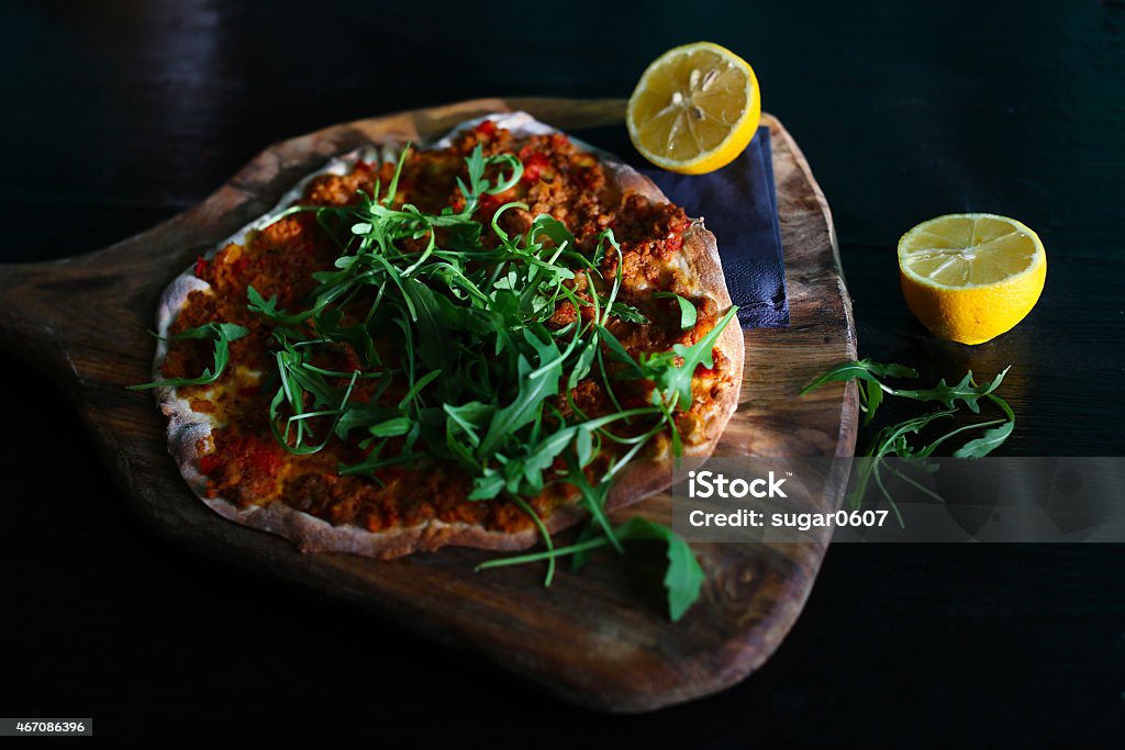 Thin turkish pizza with minced meat, lemon and arugula Thin turkish pizza with minced meat, lemon, minced bell peppers and arugula freshly baked on a wooden chopping board. 2015 Stock Photo