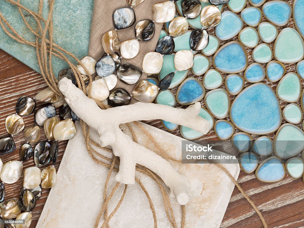 marine theme design selection of materials in a nautical theme with a blue ceramic mosaic-like sea pebbles, antique ceramic tiles, a linen cloth, pearl beads, salted wood, twine and coral 2015 Stock Photo