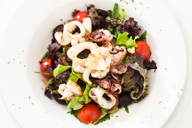 Thai squid chili salad with spices and herbs served on a white plate close up