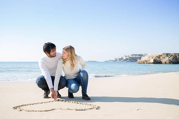 Beautiful young couple drawing heart shape in the sand, selective focus