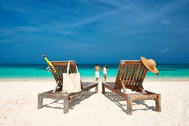 istock Two deck chairs with beach gear and couple walking on beach 467096886
