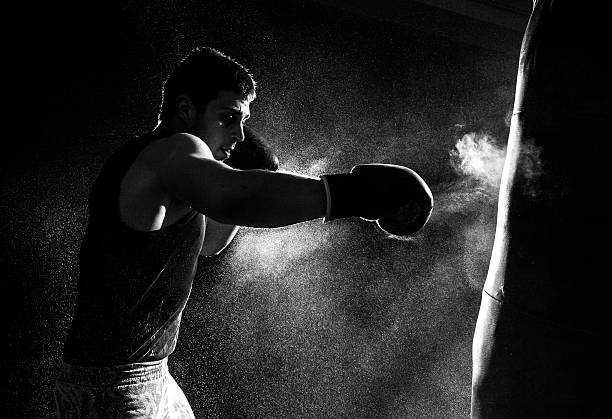 Greyscale image of a boxer having a go at the punching bag Young man boxing fighting photos stock pictures, royalty-free photos & images