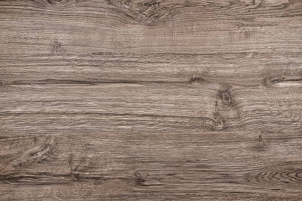 Directly above view of a light brown wood background.  This background features a distinguished wood grain pattern complete with light swirls, wavy lines and occasional knots. The color of the wood appears darker near the top and bottom, but becomes lighter near the middle. A small knot is visible near the center. Another small knot is visible in the middle of the bottom.