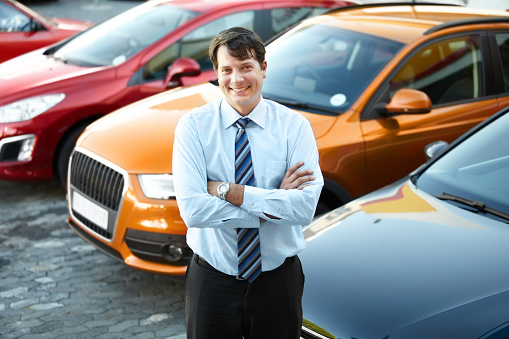 A man smiling proudly while standing in the lot of his dealership
