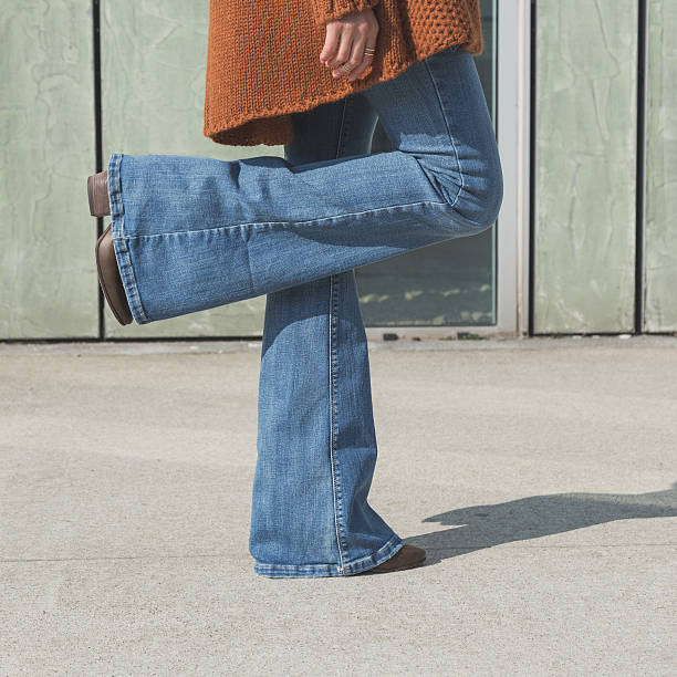 Woman in blue jeans standing on one foot on cement floor Detail of a girl wearing flared jeans and posing in an urban context flare pants stock pictures, royalty-free photos & images