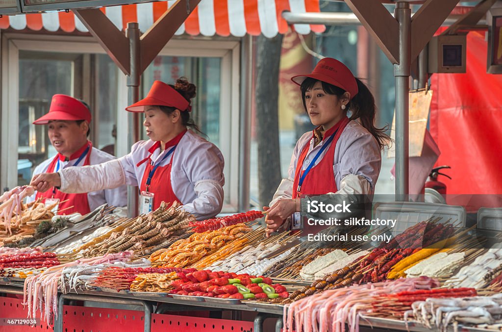 Stalls with vendors at Wangfujing snack street in Beijing Beijing, China - March 26, 2013: Stalls with vendors selling seafood and meat to be fried and served on a stick at the Donghuamen Night Market - the most popular snack street in Beijing - located at the northern entrance of Wangfujing Street. 2015 Stock Photo