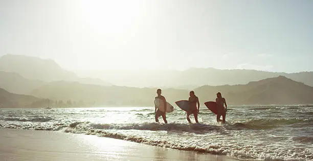 Three people walking out of the ocean and up onto a beach with surfboards in a tropical climate.