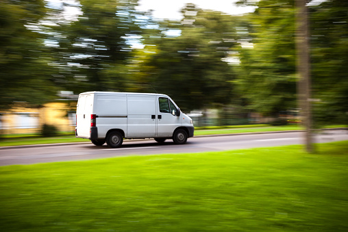 White delivery van speeding on road with blurred countryside panorama in background.