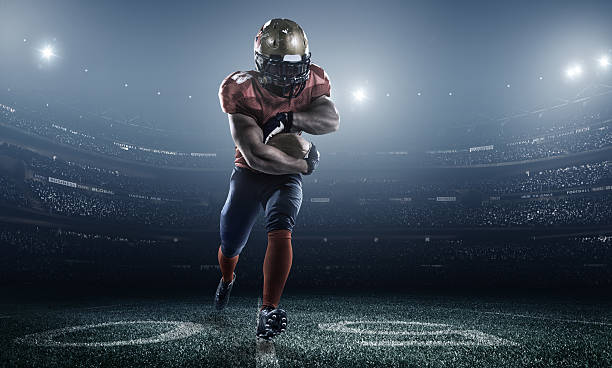 Football player running with the ball in his hand American football player with a red uniform, in dark stadium with full of spectators under night sky Touchdown stock pictures, royalty-free photos & images