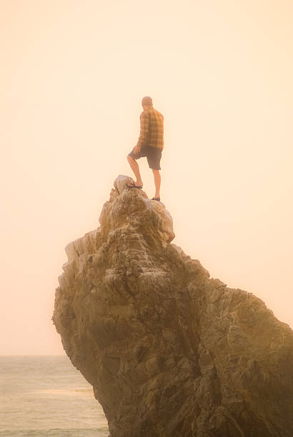 nature lover landscape a man standing on a high rock pinnacle throws his arms up into the sky in appreciation of the beautiful nature scenery that surrounds him.  horizontal composition taken at el matador beach in malibu, california. rock sea malibu silhouette stock pictures, royalty-free photos & images