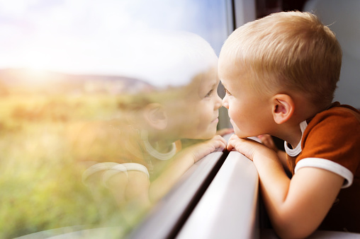 Little boy traveling in train looking outside the window.